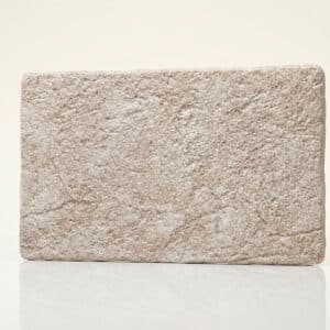 Pieza de mármol beige con textura rugosa y forma rectangular.