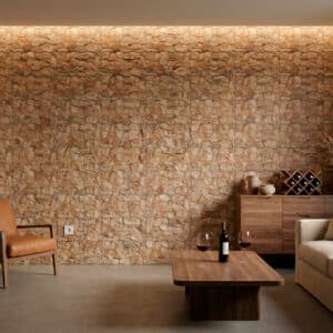 Sala de estar con estilo rústico, revestimiento de pared en piedra natural de tonos ocres y marrones, sofá beige, mesa de madera, silla de cuero marrón. La iluminación empotrada resalta la textura de la piedra.