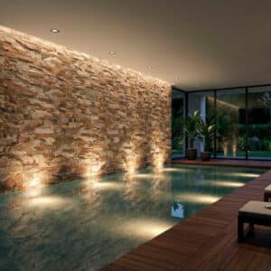 Espacio interior con piscina, estilo rústico, revestimiento de piedra marrón. Suelo de madera y plantas.