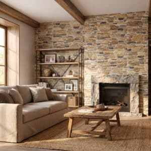 Sala de estar con estilo rústico, revestida con piedra natural de colores marrón y gris, con chimenea de piedra, sofá beige y mesas de madera. La iluminación natural entra por una ventana grande.