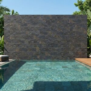 Espacio exterior con piscina de agua cristalina y pared de piedra rústica oscura, sillas de playa y vegetación tropical alrededor.