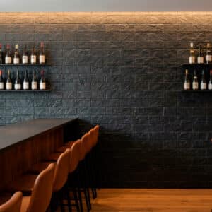 espacio interior con estilo rústico, revestimiento de piedra negra tipo catai en la pared, barra de madera y taburetes de cuero marrón