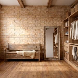 Espacio interior con suelo de madera, pared de ladrillo marrón claro, banco de madera y estanterías con ropa y accesorios. El estilo es rústico y acogedor.