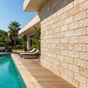 espacio exterior con piscina rectangular de agua turquesa, rodeada de madera y piedra beige, con sillas de lounge y palmeras al fondo